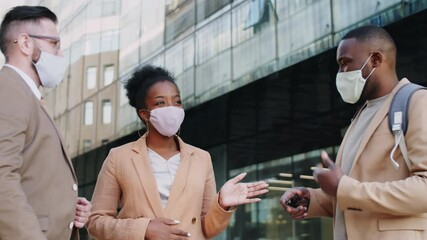 Group of multiethnic male and female colleagues in protective face masks standing outdoors on urban street and discussing business during coronavirus pandemic - Powered by Adobe