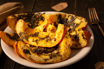 Baked pumpkin in a plate, pieces of pumpkin with dill and parsley, spices and lemon juice baked in foil in the oven