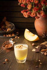 Refreshing delicious melon smoothie with cinnamon, hazelnuts and chocolate, vase of chrysanthemums and glasses of smoothie on wooden background