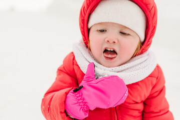 Happy laughing toddler girl wearing a red down jacket and white knitted hat and scarf playing and running in a beautiful snowy winter park on Christmas day.