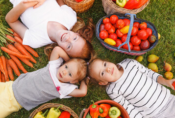 girls lie on their backs and laugh on the grass among bright vegetables