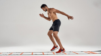 Never stop. Full length shot of young athletic man training on agility ladder drill isolated over grey background