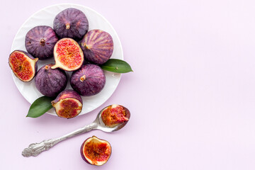Fresh whole and sliced figs on a plate with green leaves. Top view