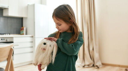 A cute small girl holding and pesting her toy dog under her arm