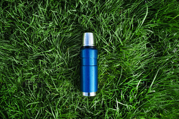 Blue vacuum thermos on green grass, top view. The concept of hiking, outdoor recreation, tourism.