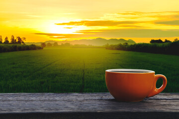 Hot coffee cup Ceramic brown glass placed on an outdoor old wood table. The background is a landscape of nature with mountains and rice field