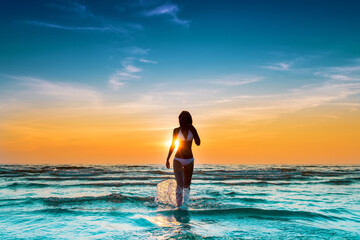 woman in white bikini posing in a sea at sunset