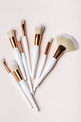 top view of white and golden cosmetic brushes set on beige background