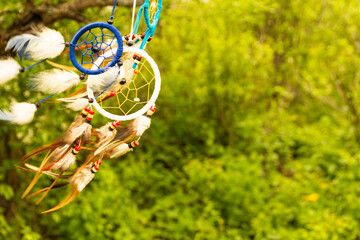Dream catchers evolve in the wind, against a blurred green background of plants with copy space,...
