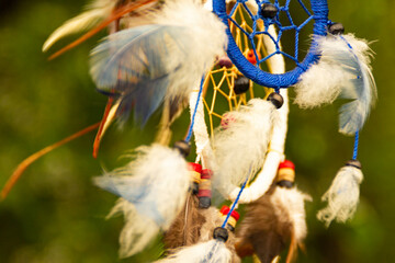 Dream catchers evolve in the wind, against a blurred green background of plants with copy space,...