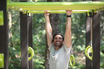 man doing abdominal exercise on horizontal bar in summer park