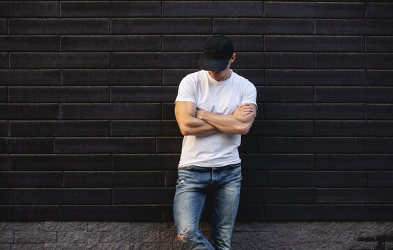Man in white t-shirt standing against brick wall with arms crossed