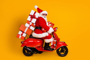 Fototapeta Profile side view of his he nice funny cheery amazed St Nicholas riding moped hurry up delivering pile stack giftboxes December winter isolated bright vivid shine vibrant yellow color background obraz