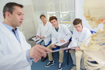 Obraz premium Teacher pointing to skeleton while giving lecture to students