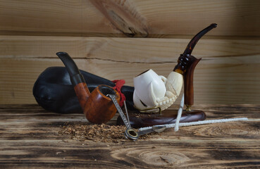 Two Smoking pipes on a stand, a tobacco pouch, pipe cleaning supplies, and tobacco crumbs on the table.