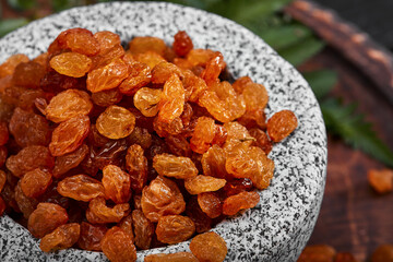 Close up of yellow raisins in a stone bowl, close up, dark background