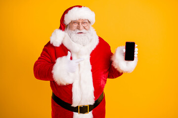 Photo grey white hair beard overweight santa claus point gloves finger smartphone recommend x-mas christmas noel tradition discount wear red cap headwear isolated yellow color background