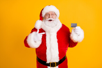 Photo excited grey white beard hair santa claus shopper point finger credit card recommend buy x-mas eve tradition christmas discount wear cap headwear isolated bright shine color background