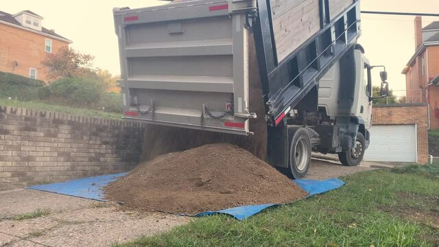 A dump trunk unloads four yards of clean topsoil dirt on a residential driveway.  	