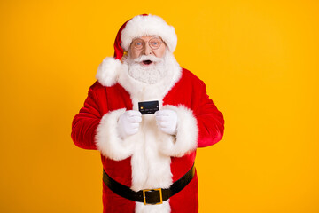 Fototapeta na wymiar Portrait of his he nice cheerful cheery funny amazed glad white-haired Santa holding in hands using black bank card isolated bright vivid shine vibrant yellow color background
