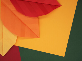 Paper origami leaves on autumn themed paper background in yellow, green, and red