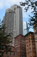 Fototapeta premium Tall residential building in the middle of Boston between some red brick houses and more skyscrapers with blue slightly cloudy sky