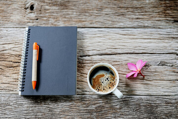 Black notebook with coffee cup and flower on old wooden table top view
