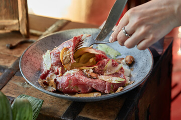 A female hand is preparing a vegetable salad with beef roast beef. A plate of salad with beef roast beef, onions, arugula, pepper and tomatoes on a black table. Top view.