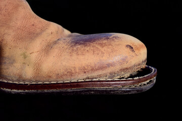 Close-up of an old leather shoe with a drooping sole, against a dark background