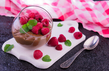 Chocolate pudding with raspberries and mint in a round glass on a dark background.