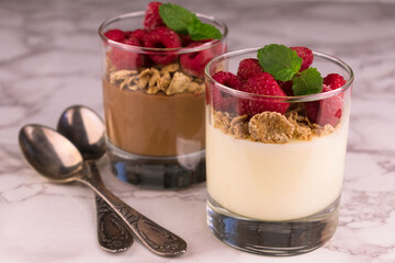 Two glasses with vanilla and chocolate pudding decorated with raspberries on the table.
