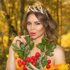 Portrait of a young beautiful woman in a dress made of autumn leaves in the park in autumn season with bouquet of flowers in her hands. Art photo