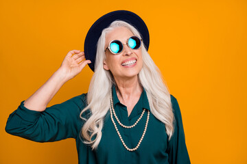 Photo of pretty cheerful white haired grandma lady senior party cool look hold touch hand retro trendy hat wear green shirt sun specs necklace isolated bright yellow color background