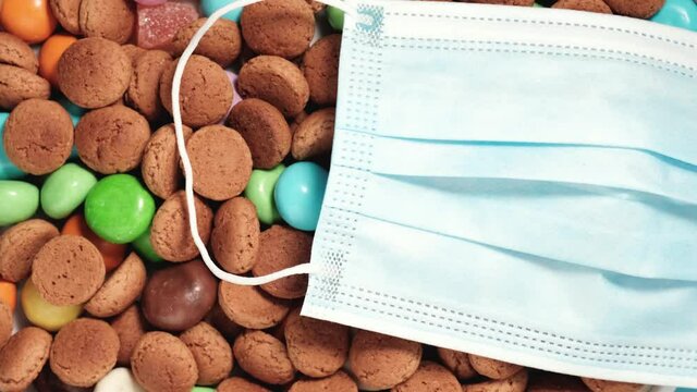 Disposable protective medical face mask with traditional dutch cookies kruidnoten. Overhead shot of Dutch holiday Sinterklaas Saint Nicholas day during covid-19 pandemic in the Netherlands, rotating