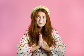 Beautiful woman praying over pink background. Girl in cute outfit begging someone with hope in eyes to satisfy her desires, help with.