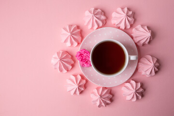 A cup of tea on a delicate pink background with pink meringues.