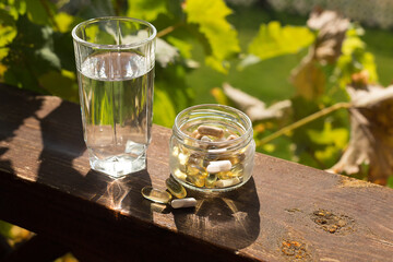 Vitamins for health pills set in a jar and a glass of water in the sun.