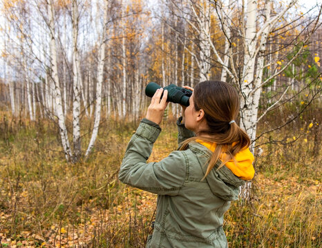 Young woman with binoculars watching birds in the autumn forest. Scientific research