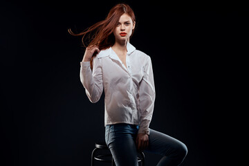 pretty woman sitting on a chair posing white shirt jeans long hair red lips dark background