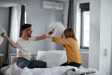 Boyfriend and girlfriend fighting pillows on the bed. Happy couple having fun at home..