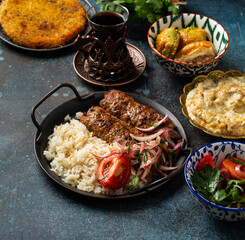 Traditional Turkish dish meat kebab with rice, vegetables served with appetizers and Turkish tea in glass. Kebab, eggplant sauce, pita bread, dessert Künefe and baklava. Middle Eastern meal close-up