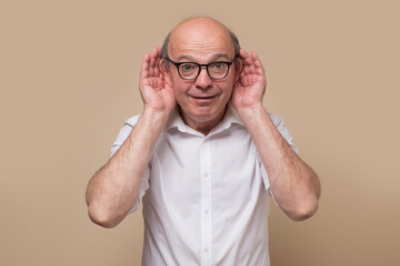 Senior bald male adult in glasses listening carefully, spying, being curious. Studio shot