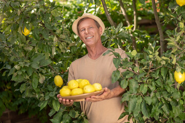 Obraz premium Smiling male in straw hat holding plate with lemons