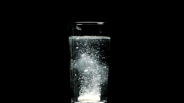 White Effervescent dissolving aspirin pill drops into glass of water and dissolves isolated on black backdrop. Taking medication concept. Effervescent tablet, calcium, magnesium, vitamins, aspirin