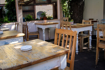 In einem Straßenkaffee sind einige Holzstühle und Holztische aufgestellt.