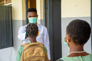 teacher in a school checking pupils body temperature before they enter the classroom
