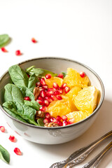 Bright fruit salad close-up. Salad of oranges, pomegranate, spinach and nuts in a bowl on a white background. Free space for text. Healthy diet food, vegetarian food. Copy space.