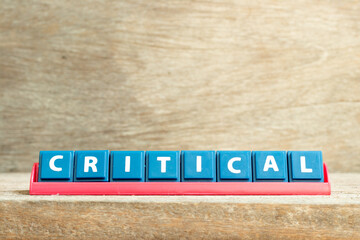 Tile letter on red rack in word critical on wood background