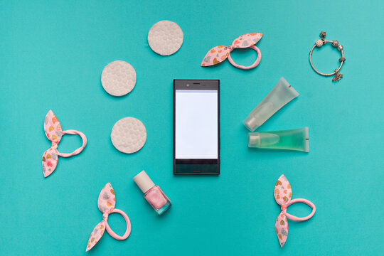 Phone, Pink Hair Ties With Bows, Hand Decoration, Cream, Shampoo, Nail Polish, Face Cleaning Discs On A Blue Background. View From Above. Women's Accessories.