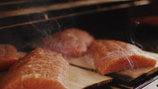 smoked salmon filets on little wooden planks roasting on a grill steaming and are ready to be eaten